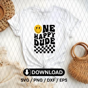 May include: White t-shirt with a black and yellow graphic design. The graphic features a smiley face with lightning bolts, the text "One Happy Dude", and a checkered pattern.