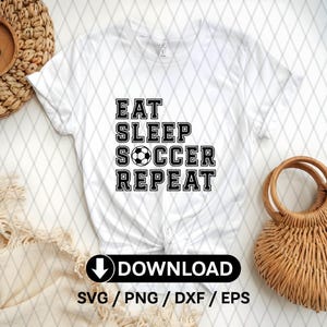 Op de afbeelding: Wit T-shirt met zwarte tekst die "Eat Sleep Soccer Repeat" zegt en een zwart-witte voetbalafbeelding.