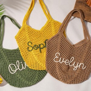 K&ouml;nnte beinhalten: Drei geh&auml;kelte Tragetaschen in Olivgr&uuml;n, Gelb und Braun. Jede Tasche hat einen Namen in Wei&szlig; gestickt: "Olivia", "Sophie" und "Evelyn". Die Taschen haben lange Henkel und ein netzartiges Gewebe.