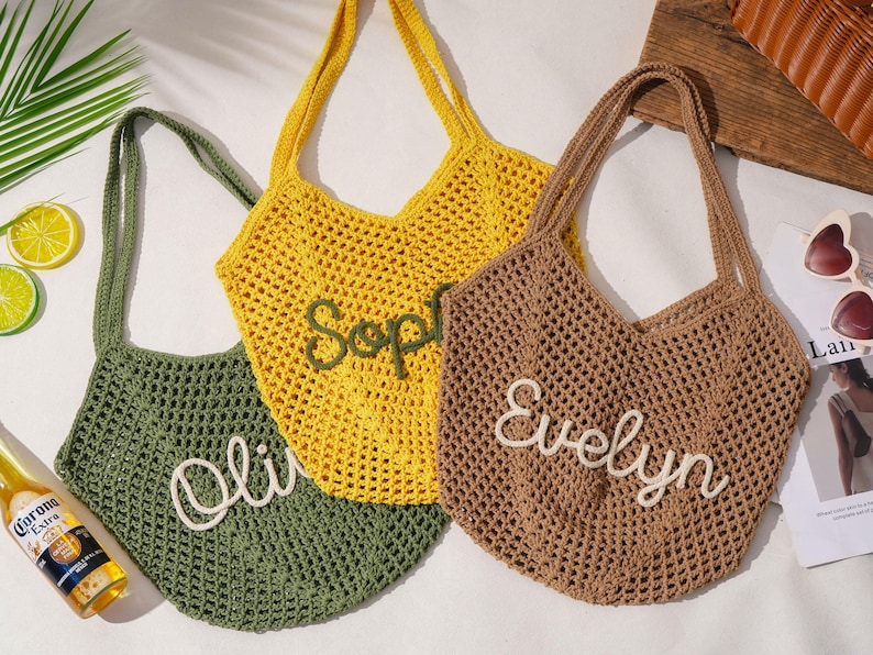 K&ouml;nnte beinhalten: Drei geh&auml;kelte Tragetaschen in Olivgr&uuml;n, Gelb und Braun. Jede Tasche hat einen Namen in Wei&szlig; gestickt: "Olivia", "Sophie" und "Evelyn". Die Taschen haben lange Henkel und ein netzartiges Gewebe.