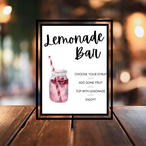 Puede incluir: Un cartel blanco con texto negro que dice "Lemonade Bar". El cartel tiene una ilustración de acuarela de un tarro de vidrio lleno de limonada rosa y una pajita a rayas rojas y blancas. El texto debajo de la ilustración dice "Elige tu jarabe, Agrega algo de fruta, Cúbrelo con limonada, ¡Disfruta!"