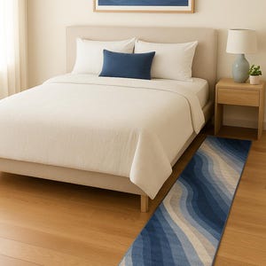 Könnte beinhalten: Ein Schlafzimmer mit einem Bett, weißer Bettwäsche und einem marineblauen Kissen. Ein gerahmtes Kunstwerk mit blauen Wellenmustern hängt über dem Bett. Ein langer, schmaler Teppich mit einem Wellendesign in Blau- und Beigetönen liegt auf dem Holzboden.