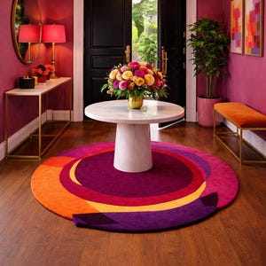 Può includere: Scena d'interni vivace con un tappeto rotondo con cerchi concentrici nei toni del viola, arancione e giallo. Un tavolo in marmo bianco ospita una composizione floreale. La stanza ha pareti magenta, un lampadario e una panca.