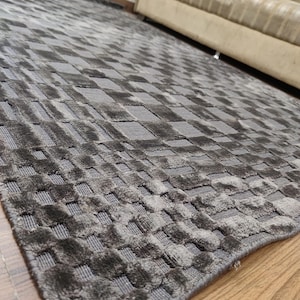 May include: A gray area rug with a woven, checkered pattern. The rug's design features a repeating square motif, creating a textured surface. The rug is made of a soft material and is suitable for living rooms and bedrooms.