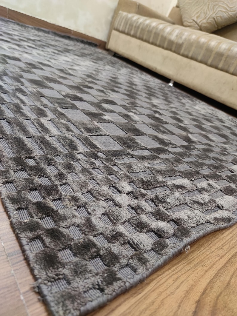 May include: A gray area rug with a woven, checkered pattern. The rug's design features a repeating square motif, creating a textured surface. The rug is made of a soft material and is suitable for living rooms and bedrooms.