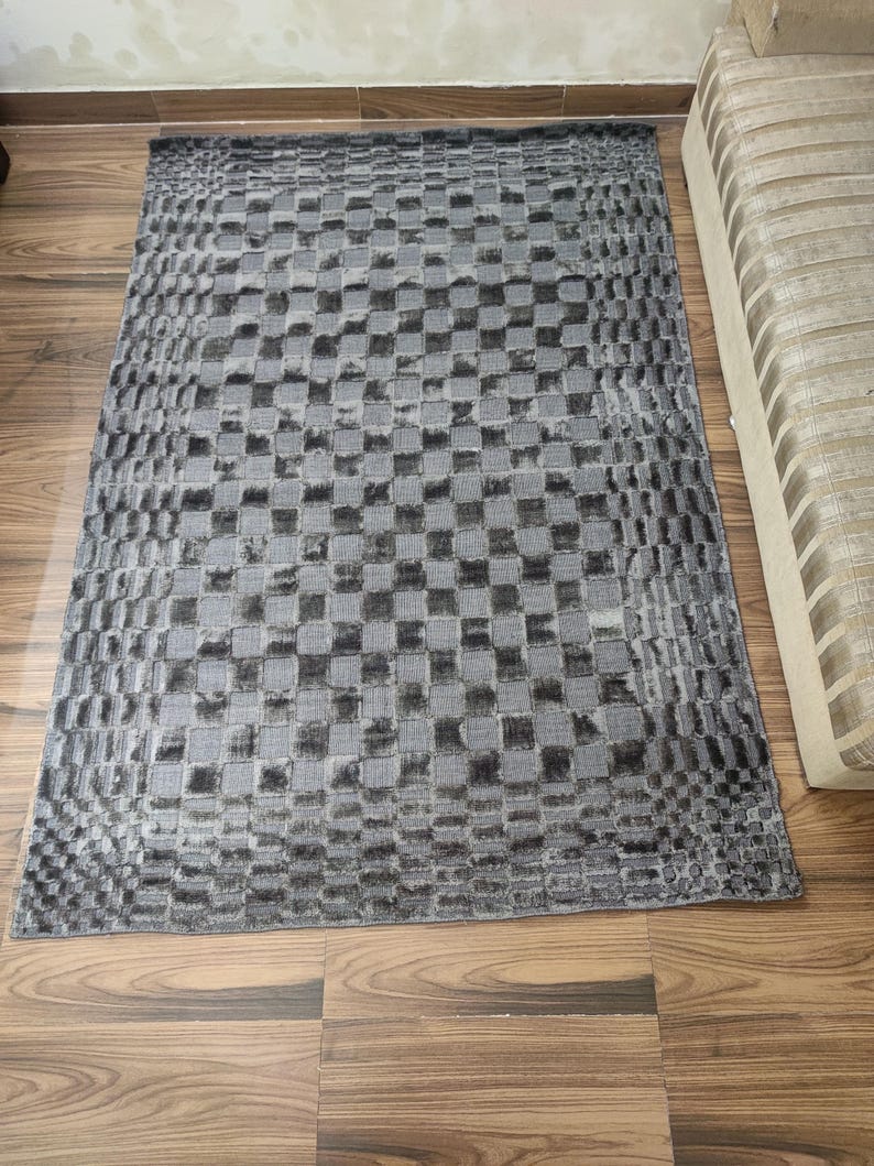 May include: A rectangular gray rug with a checkered pattern. The rug is made of a soft material and has a textured appearance. The rug is placed on a wooden floor.