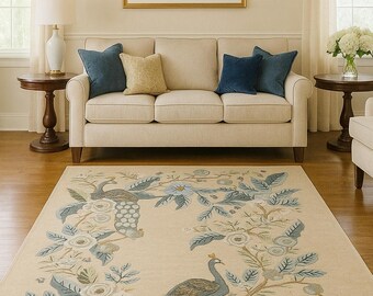 May include: Cream-coloured area rug featuring a peacock and floral design in blue, green, and tan. The rug is in a living room with a cream sofa, blue cushions, and a landscape painting.