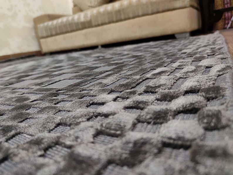 May include: A close-up shot of a gray area rug with a textured, geometric pattern. The rug's design features a series of raised, rounded shapes, creating a tactile surface. The color palette is a blend of gray tones, adding depth and dimension to the rug.