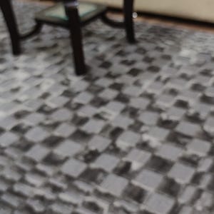 May include: A living room scene featuring a dark wood coffee table with a glass top, a beige sofa with pillows, and a gray checkered rug. The rug covers the floor in front of the sofa and table.