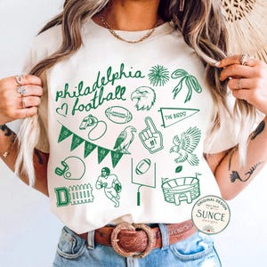 model wearing irvory comfort colors shirt that has doodle football designs and says philadelphia football