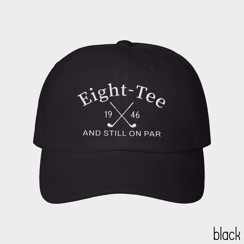 Puede incluir: Una gorra de b&eacute;isbol negra con texto bordado en blanco que dice Eight-Tee, con los n&uacute;meros 19 y 46 a cada lado de dos palos de golf cruzados, y el texto AND STILL ON PAR bordado en blanco debajo de los palos de golf.
