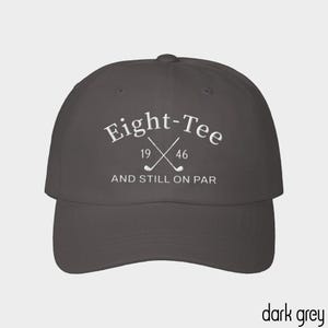 Puede incluir: Una gorra de b&eacute;isbol gris oscuro con texto bordado en blanco que dice Eight-Tee, los n&uacute;meros 19 y 46, y la frase AND STILL ON PAR. El dise&ntilde;o incluye un gr&aacute;fico de dos palos de golf cruzados centrados entre los n&uacute;meros.