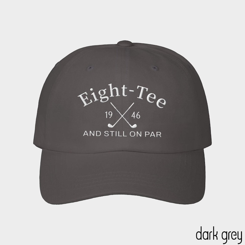 Puede incluir: Una gorra de b&eacute;isbol gris oscuro con texto bordado en blanco que dice Eight-Tee, los n&uacute;meros 19 y 46, y la frase AND STILL ON PAR. El dise&ntilde;o incluye un gr&aacute;fico de dos palos de golf cruzados centrados entre los n&uacute;meros.