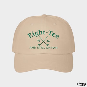 Puede incluir: Una gorra de b&eacute;isbol color piedra con bordado verde oscuro en la parte frontal. El texto dice Eight-Tee, 19 46 y AND STILL ON PAR, acompa&ntilde;ado de un gr&aacute;fico de dos palos de golf cruzados centrados entre los n&uacute;meros 19 y 46.