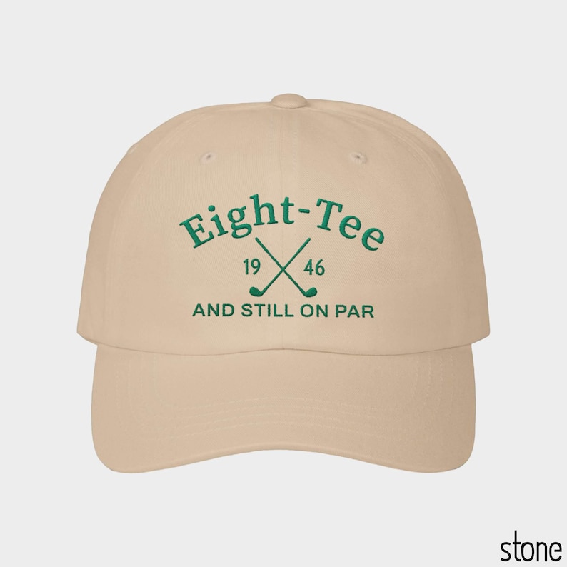 Puede incluir: Una gorra de b&eacute;isbol color piedra con bordado verde oscuro en la parte frontal. El texto dice Eight-Tee, 19 46 y AND STILL ON PAR, acompa&ntilde;ado de un gr&aacute;fico de dos palos de golf cruzados centrados entre los n&uacute;meros 19 y 46.