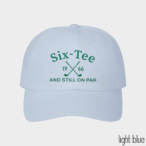 May include: A light blue baseball cap featuring dark green embroidery on the front. The text reads Six-Tee, 19 66, and AND STILL ON PAR, accompanied by a graphic of two crossed golf clubs. The cap has a structured crown and a curved brim.