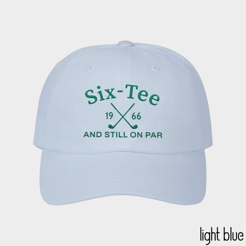May include: A light blue baseball cap featuring dark green embroidery on the front. The text reads Six-Tee, 19 66, and AND STILL ON PAR, accompanied by a graphic of two crossed golf clubs. The cap has a structured crown and a curved brim.
