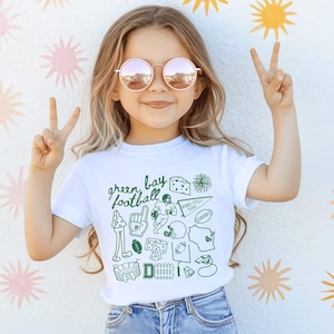 toddler models wearing white rabbit skins tee shirt with a football doodle design and says green bay football