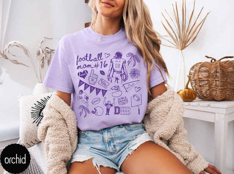May include: A light purple short-sleeve t-shirt featuring a dark purple graphic print with the text football mom #16, a football player with the number 16, a foam finger, a pennant, a whistle, a stadium, a goal post, and various football icons.