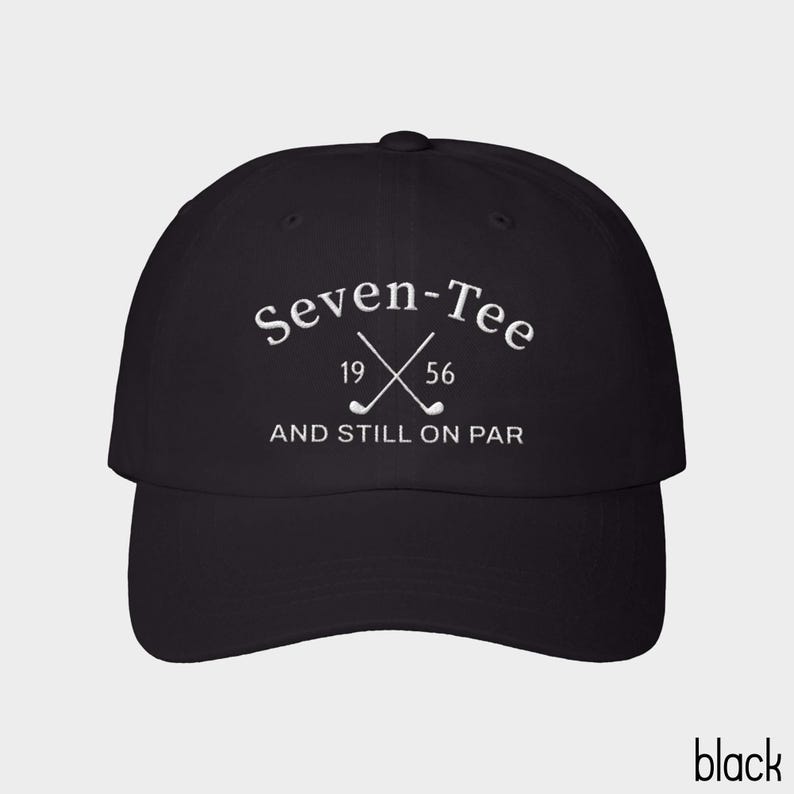 May include: A black baseball cap featuring white embroidered text that reads Seven-Tee 19 56 AND STILL ON PAR, with a graphic of two crossed golf clubs positioned between the numbers 19 and 56 on the front panel of the hat.