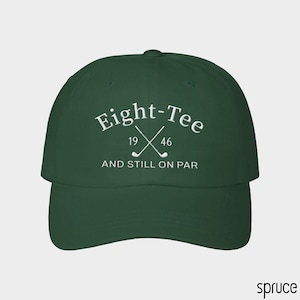 Puede incluir: Una gorra de b&eacute;isbol de color verde oscuro con texto bordado en blanco que dice Eight-Tee, 19 46 y AND STILL ON PAR, junto con un gr&aacute;fico de dos palos de golf cruzados situados entre los n&uacute;meros 19 y 46 en el panel frontal.