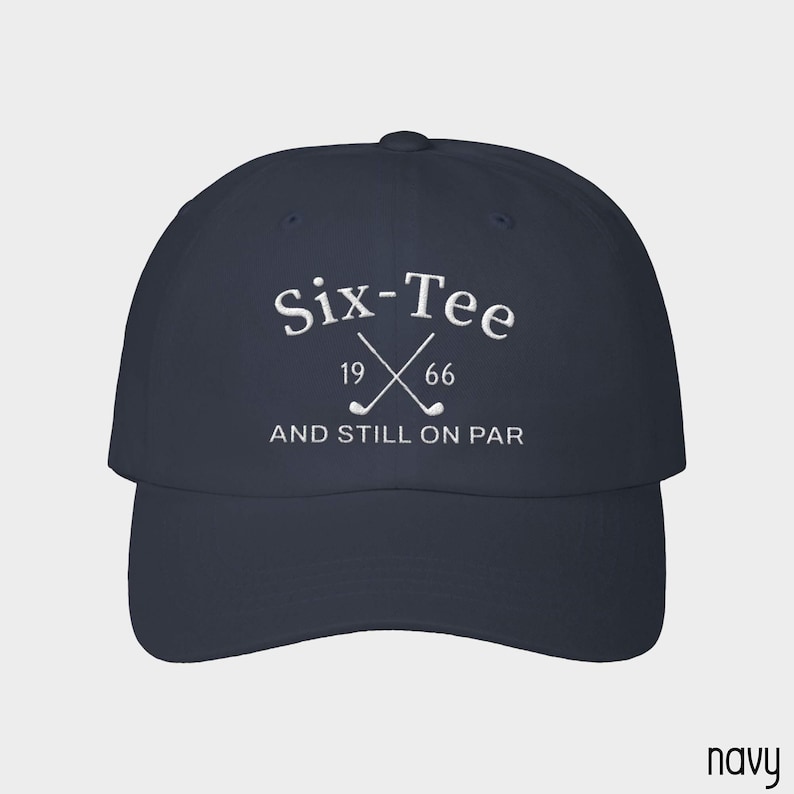 May include: A navy blue baseball cap featuring white embroidered text that reads Six-Tee 19 66 AND STILL ON PAR, with a graphic of two crossed golf clubs positioned between the numbers 19 and 66 on the front panel of the hat.