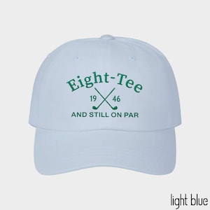 Puede incluir: Una gorra de b&eacute;isbol azul claro con bordado verde oscuro en la parte delantera. El texto dice Eight-Tee con los n&uacute;meros 19 y 46 flanqueando dos palos de golf cruzados, seguido del texto AND STILL ON PAR centrado debajo de los palos.