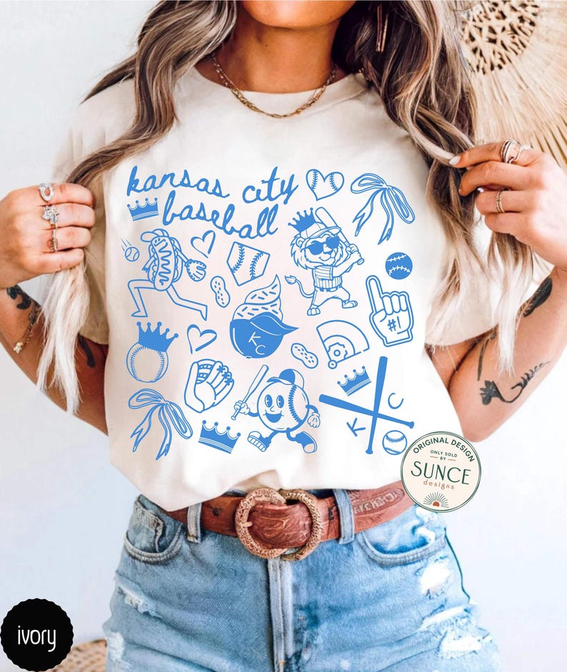 model wearing ivory comfort colors shirt that says kansas city baseball and has a baseball doodle design