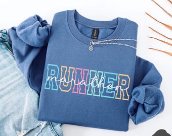 May include: A blue sweatshirt with the text "RUNNER marathon" in rainbow colors. The sweatshirt has a relaxed fit and a crew neck.