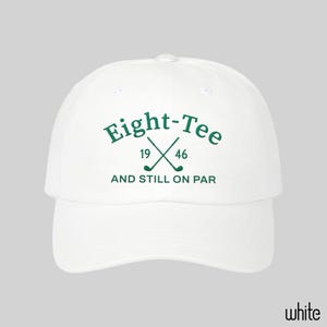 Puede incluir: Una gorra de b&eacute;isbol blanca con texto bordado en verde oscuro que dice Eight-Tee, 19 46 y AND STILL ON PAR, junto con un gr&aacute;fico de dos palos de golf cruzados situados entre los n&uacute;meros 19 y 46 en la parte frontal de la corona.
