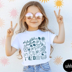 toddler model wearing white rabbit skins tee shirt with a football doodle design and says philadelphia football