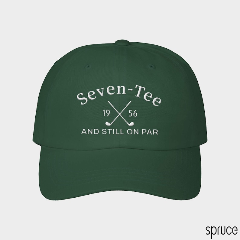 May include: A dark green baseball cap featuring white embroidered text that reads Seven-Tee 19 56 AND STILL ON PAR, accompanied by a graphic of two crossed golf clubs centered between the numbers 19 and 56 on the front panel of the hat.