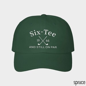 May include: A dark green baseball cap featuring white embroidered text that reads Six-Tee 19 66 AND STILL ON PAR, with a graphic of two crossed golf clubs positioned between the numbers 19 and 66 on the front panel of the hat.