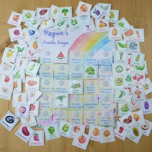 Könnte beinhalten: Ein Satz bunter illustrierter Karten mit verschiedenen Früchten und Gemüsesorten. Die Karten sind in einem Kreis um eine Bingokarte mit dem Titel "Raquet's Foodie Bingo" angeordnet.