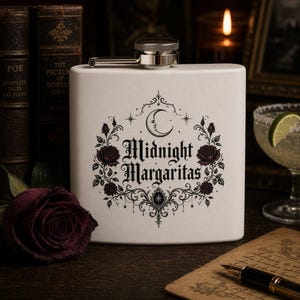 May include: A white rectangular flask with a silver cap and spout. The flask features a black and white gothic design with the words "Midnight Margaritas" surrounded by roses and a crescent moon.
