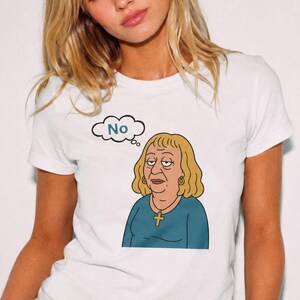 May include: A white short-sleeved t-shirt featuring a cartoon illustration of a blonde person with a gold cross necklace wearing a teal shirt. Above the character is a thought bubble containing the word No in blue text on a white background.