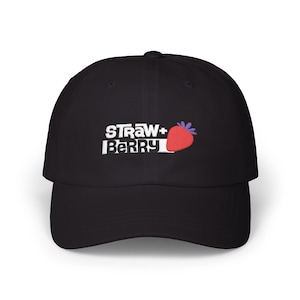 Peut inclure: Casquette de baseball noire avec l'inscription "STRAW+BERRY" en blanc et une fraise rouge avec des feuilles violettes. La casquette a une visière incurvée et une fermeture à sangle en tissu.