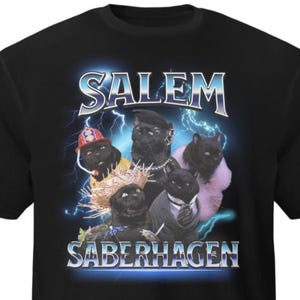 May include: Black t-shirt with a graphic of five black cats in costumes, including a firefighter's hat and a suit. The words "SALEM" and "SABERHAGEN" are in a silver, stylized font with a lightning bolt effect.