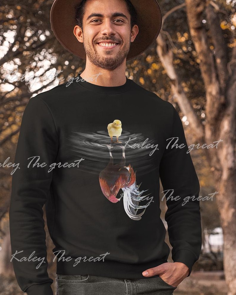 May include: A black sweatshirt with a graphic of a chicken and a chick. The graphic shows the chicken upside down in water with the chick standing on the water's surface. The text "Kaley The Great" is printed on the sweatshirt.