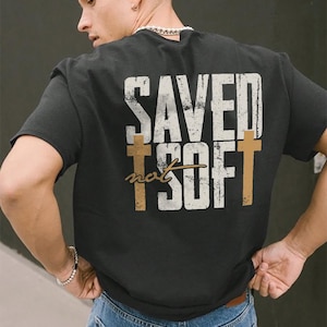 May include: Black t-shirt with a white graphic that says "SAVED not SOFT" with a cross on either side of the text.