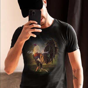 Puede incluir: Una camiseta negra con una imagen colorida de un gallo con el texto "Kaley The Great" impreso en la parte delantera.