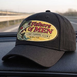 K&ouml;nnte beinhalten: Schwarze Baseballkappe mit gebogenem Schirm. Auf der Kappe befindet sich ein Aufn&auml;her mit dem Text "Fishers of Men Pro Fishing Club Matthew 4:19" und einer Grafik eines aus dem Wasser springenden Fisches.