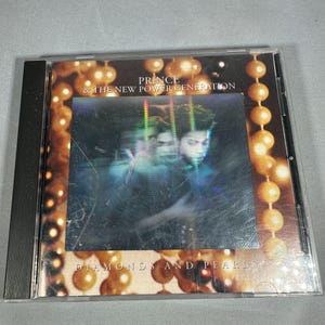 May include: A CD case for the album "Diamonds and Pearls" by Prince & The New Power Generation. The cover features a blurred image of Prince with a background of gold-colored orbs. The album title is printed in white letters.