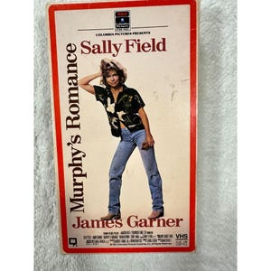 May include: A vintage VHS tape for the movie "Murphy's Romance" featuring Sally Field and James Garner. The tape has a red border with the movie title and actors' names in white. The cover shows a photo of Sally Field.