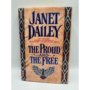 May include: A hardcover book titled "The Proud and the Free" by Janet Dailey. The cover is tan with the author's name in large blue letters. The title is in blue, with a stylized eagle graphic.
