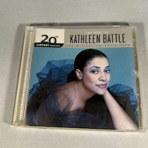 Peut inclure: Un boîtier de CD avec "The Best of Kathleen Battle: The Millennium Collection." La couverture présente un portrait de Kathleen Battle dans une image aux tons bleus. Le texte "20th Century Masters" est également visible.