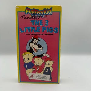 Puede incluir: Una caja de cinta VHS vintage para la caricatura "Los 3 cerditos". La caja es amarilla con un panel central rosa con ilustraciones de dibujos animados de los tres cerdos y un lobo. El texto incluye "Funtime Kid" y "Plus 3 More Color Cartoons!"