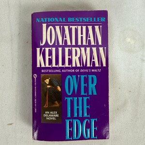 May include: A paperback book titled "Over the Edge" by Jonathan Kellerman. The cover is a deep purple with white text that reads "National Bestseller" and the author's name. The title is in large, turquoise letters. An image of a person is in the lower left corner.