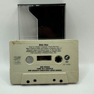 May include: A vintage cassette tape of Jim Croce's "Time in a Bottle" album. The off-white cassette features song titles and production credits. The clear plastic case is open, revealing the tape's label. The cassette is labeled "Side One".