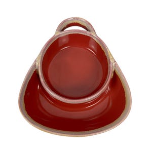 May include: A red ceramic serving dish with a built-in handle and a matching saucer base. The dish has a glossy finish with a lighter-colored rim. The handle is arched, and the overall shape is a rounded triangle.